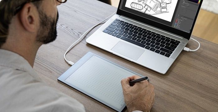 Person skissar på en digital ritplatta bredvid en laptop